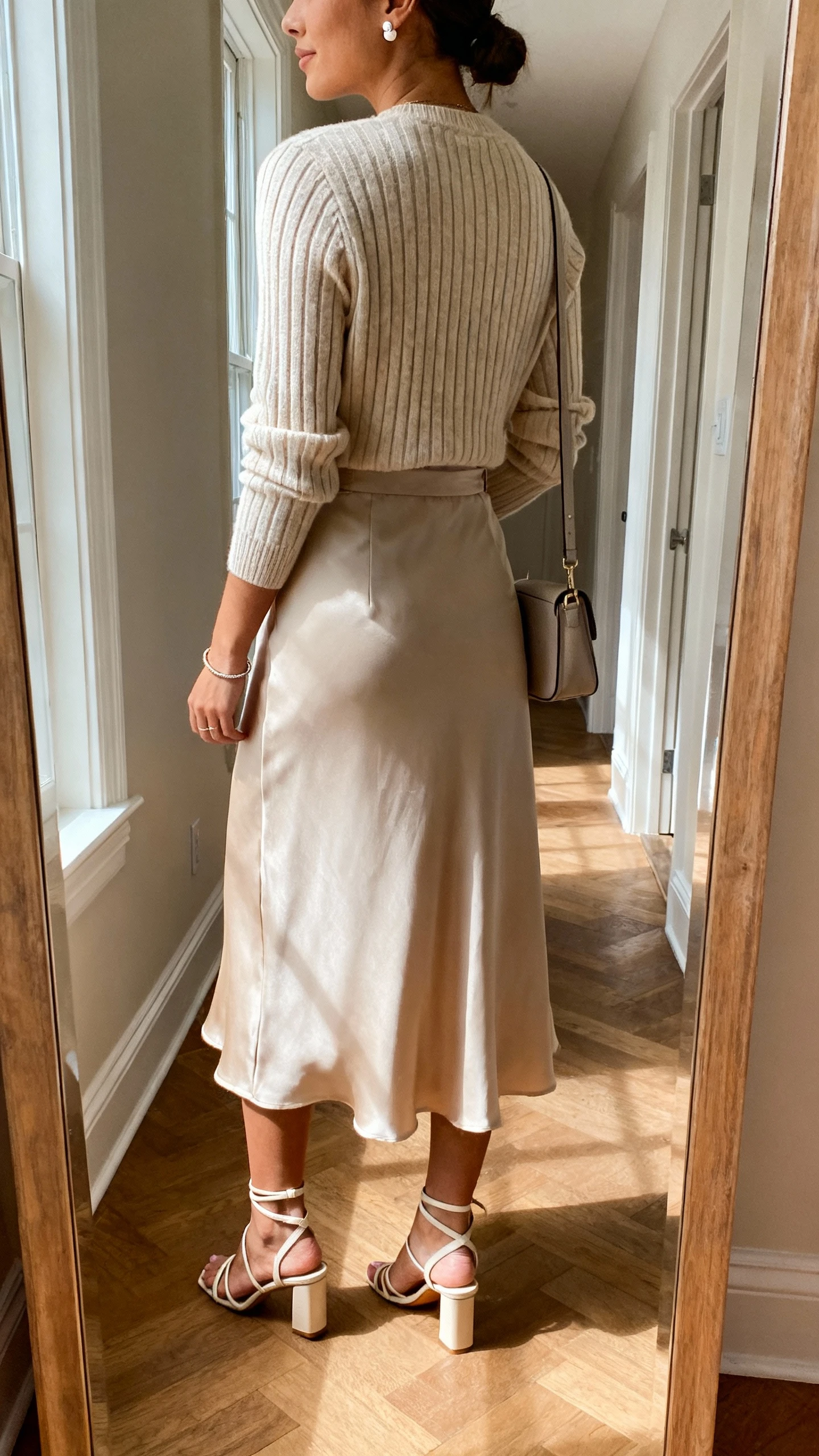 iPhone back view of a woman wearing a luxe ribbed knit sweater tucked into a fluid midi skirt, dainty stud earrings, thin bracelet, strappy heeled sandals, and a small shoulder bag, face not visible, hallway mirror, gentle afternoon window light, iPhone photo quality.