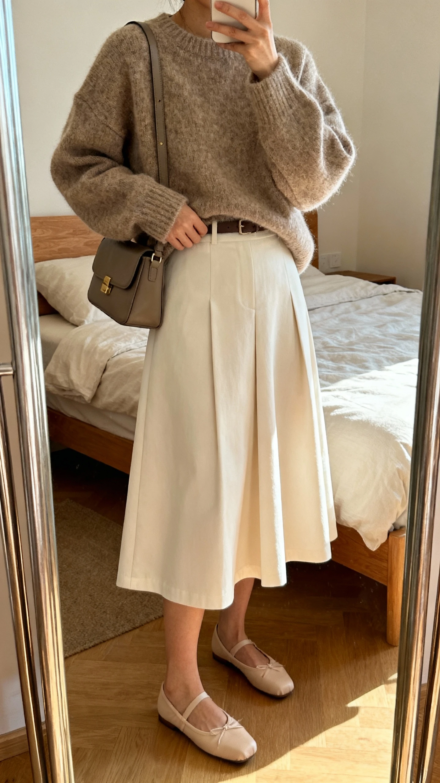iPhone mirror selfie of a woman wearing an oversized cozy sweater tucked into a crisp A-line midi skirt with ballet flats and a structured shoulder bag, face not visible, cropped at neck, bedroom mirror, warm indoor lighting, iPhone photo quality.